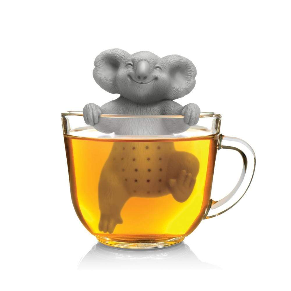 A glass teacup holds a gray koala-shaped tea infuser, which is hanging from the edge of the cup and smiling.