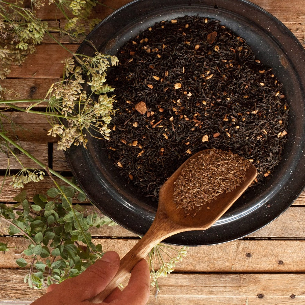 A wooden spoon scoops more spices into a bowl of blended tea and spices