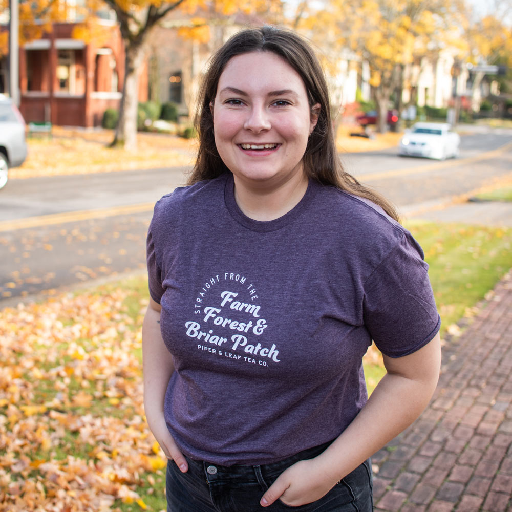 A young woman shows off her purple Piper & Leaf tea-shirt printed with: “Straight from the Farm, Forest, & Briar Patch. Piper and Leaf Tea Co.”