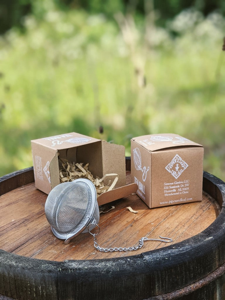 A mesh tea ball in front of two tea ball boxes